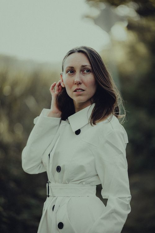 Free Portrait of an elegant woman in a white coat with long hair, capturing a fashionable outdoor look. Stock Photo