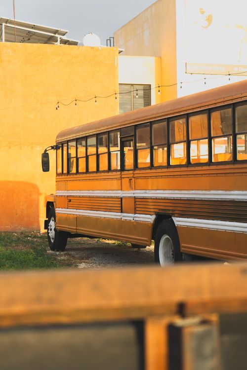Free Golden school bus parked beside a vibrant yellow wall in Mérida, Mexico, showcasing a vintage feel. Stock Photo