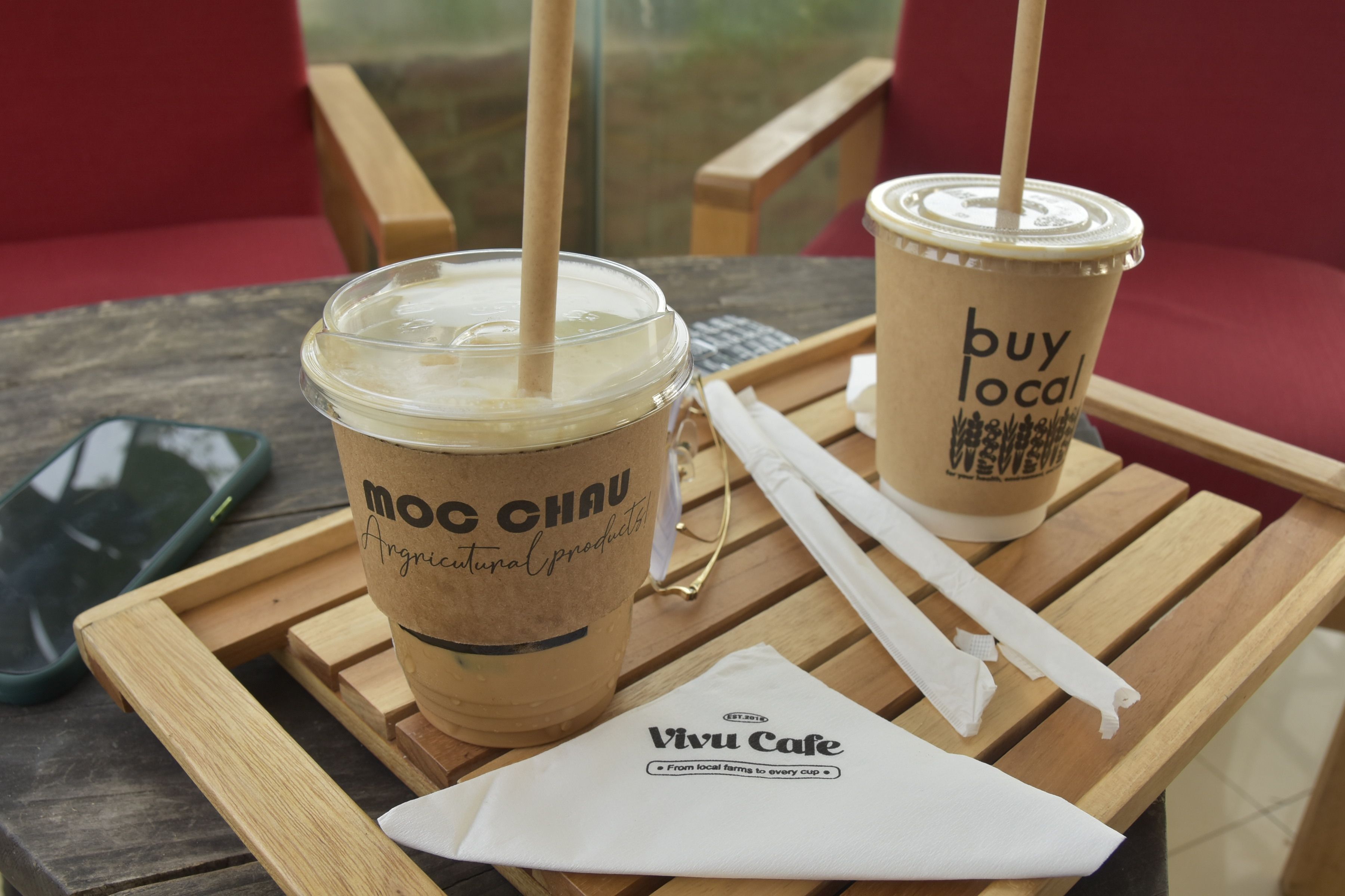 Coffee on a wooden tray with branded Moc Chau and Buy Local cups, eco-friendly setup.