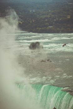Aerial view of the powerful Niagara Falls with mist and lush summer greenery.