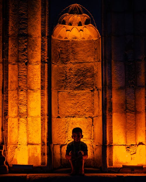 Boy Crouching in front of an Illuminated Historical Building