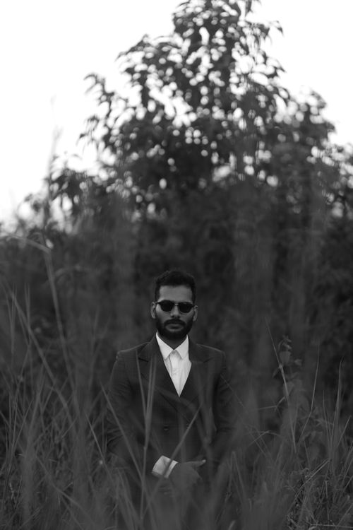 Free Black and white photo of a man in a suit and sunglasses standing in a grassy field. Stock Photo