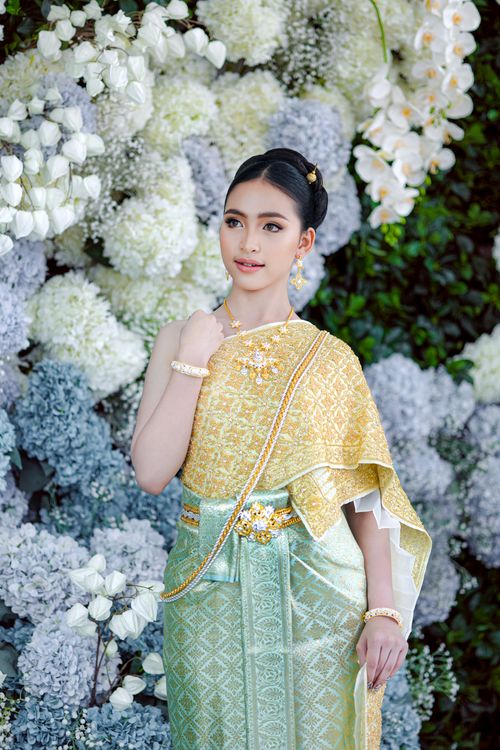 Free Portrait of a woman wearing traditional Thai dress standing against a floral backdrop. Stock Photo
