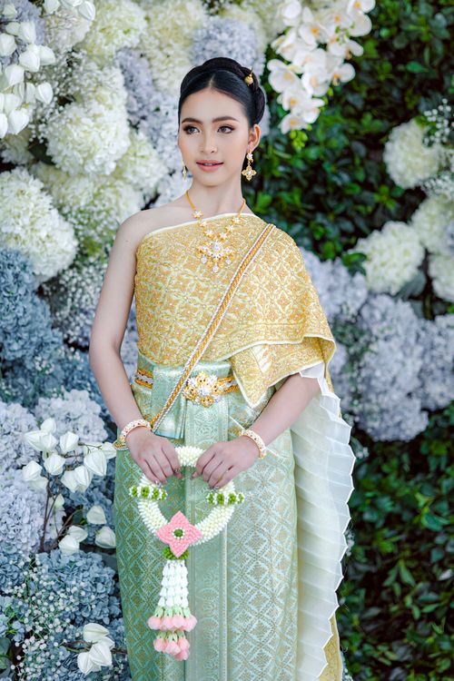 Free A woman in traditional Thai attire holding a floral garland against a floral backdrop. Stock Photo