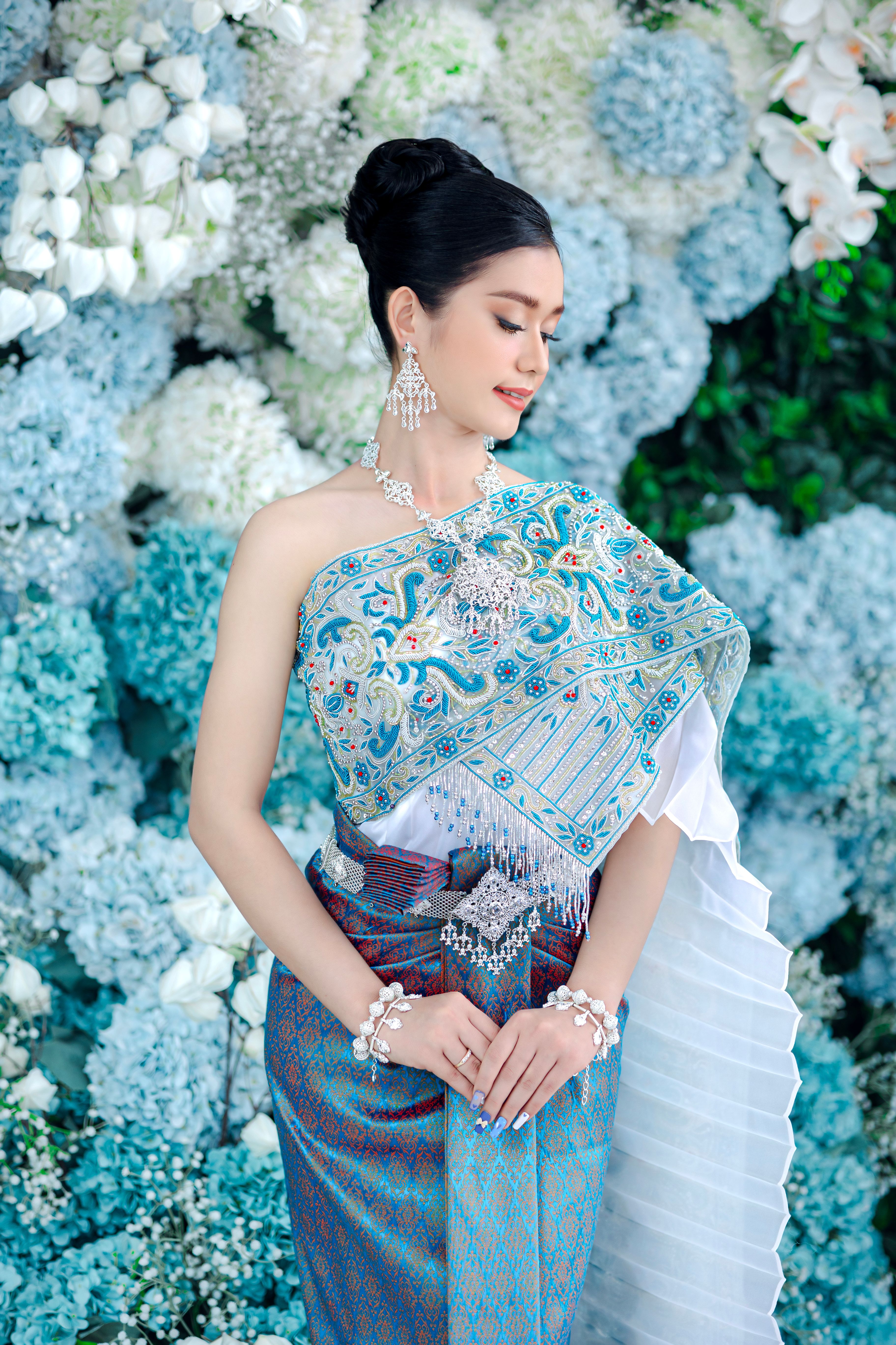 Elegant Asian woman in traditional attire posing gracefully amid a floral backdrop, embodying beauty and sophistication.