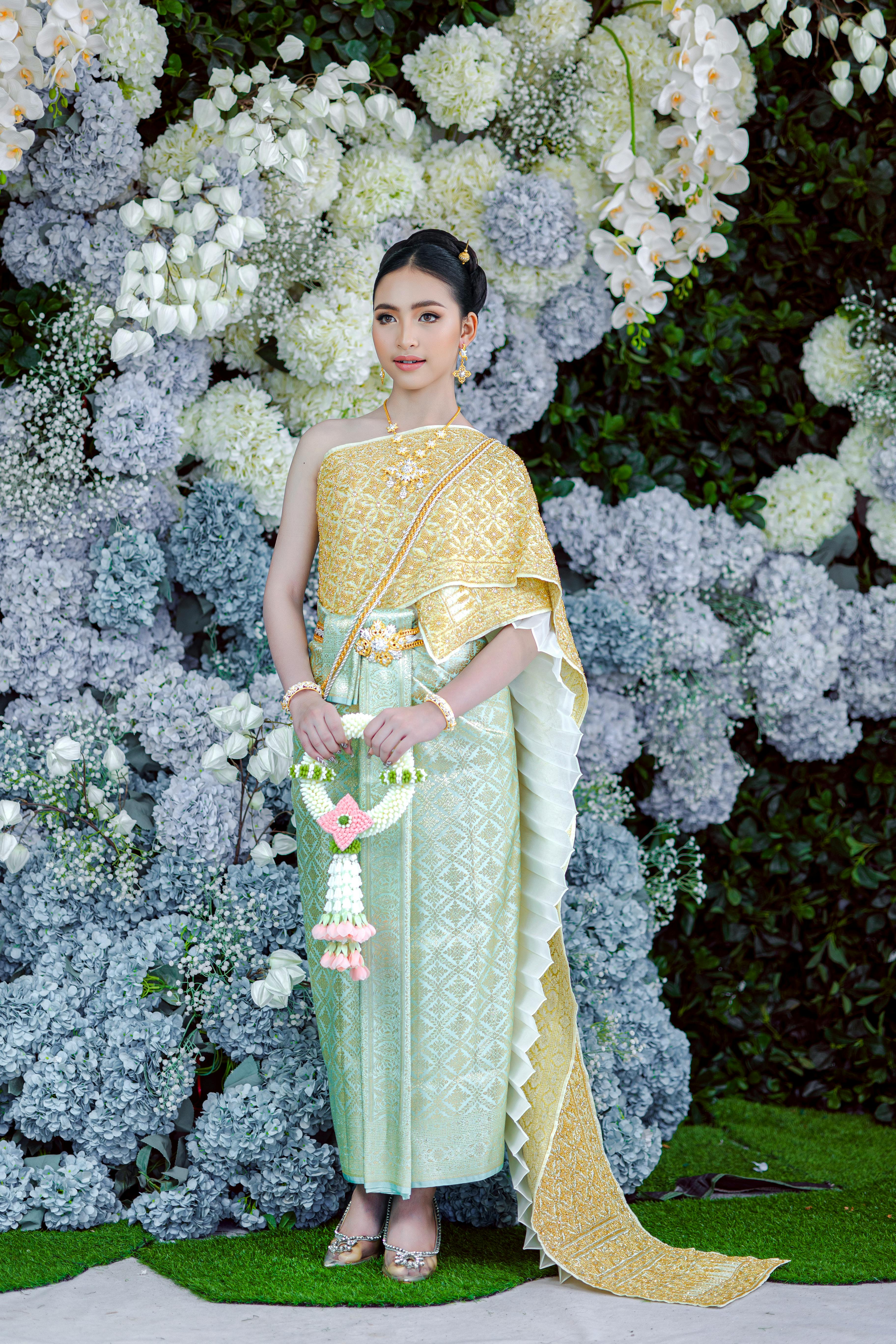 Portrait of a woman in traditional Thai clothing amidst floral backdrop, showcasing elegance and cultural heritage.