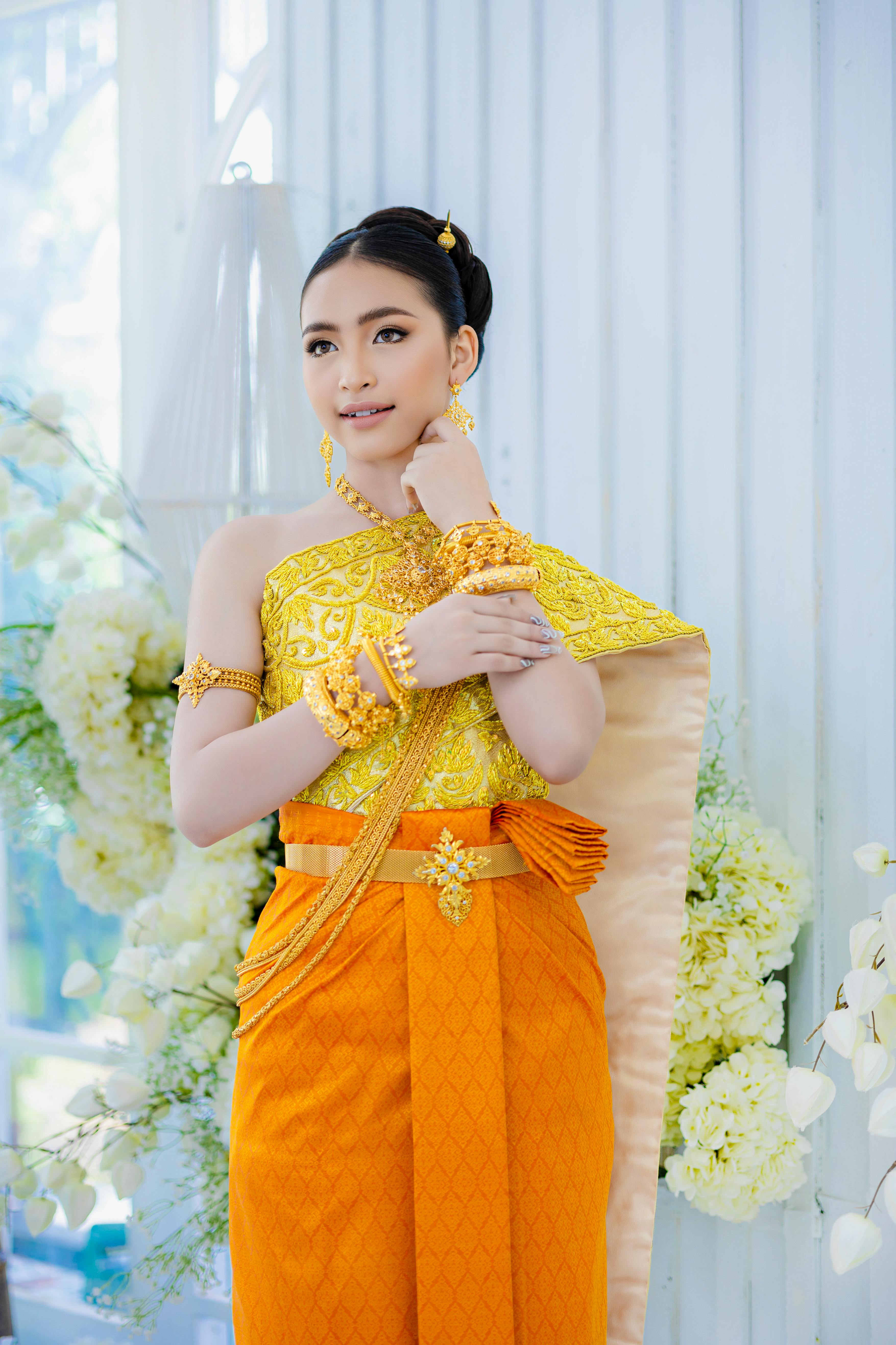 A woman elegantly poses in vibrant traditional Khmer attire indoors, perfect for weddings.