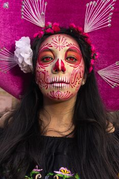 Close-up portrait of a woman with Day of the Dead face paint wearing a pink sombrero.