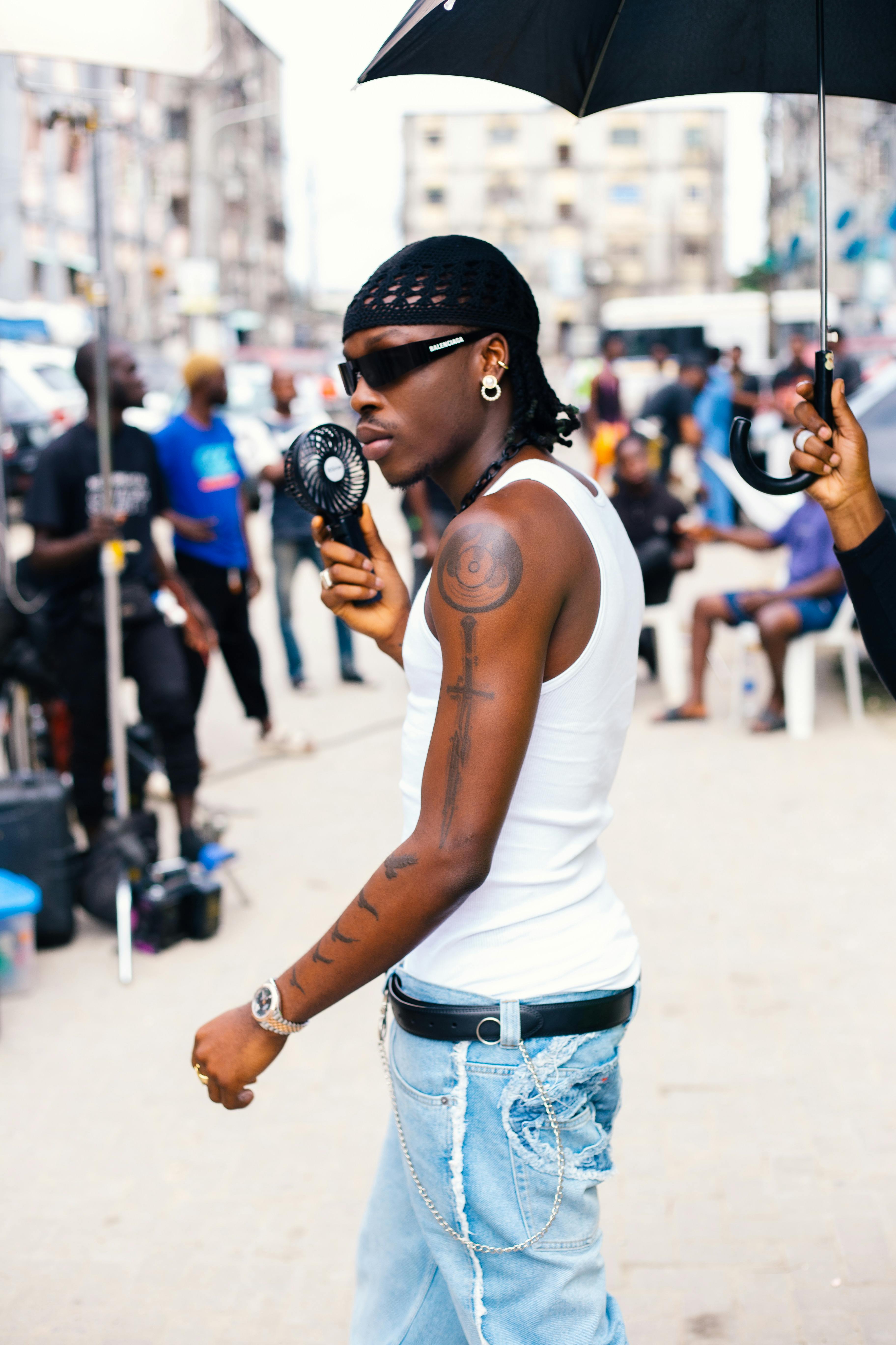 Stylish man in sunglasses with fan on Lagos street, showcasing urban fashion and culture.