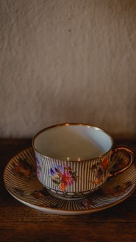 A beautifully detailed hand-painted porcelain cup and saucer on a wooden surface. — photo by tomris