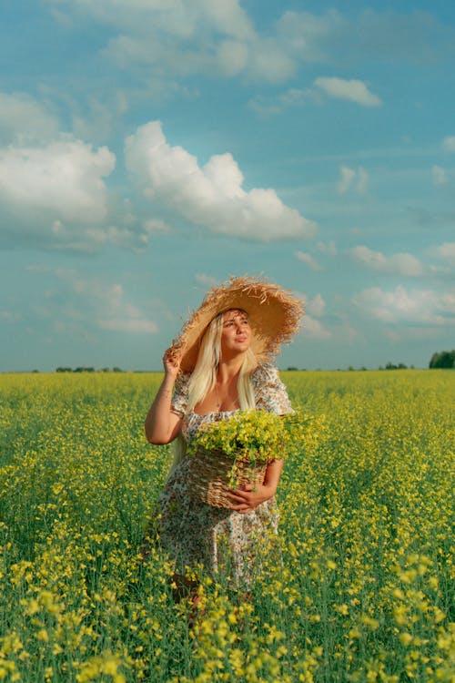 Young woman in a Dress and Hat Standing in a Canola Field in Summer 