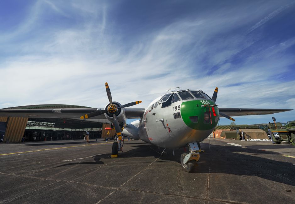 A military aircraft parked outdoors on an airbase under a bright blue sky.