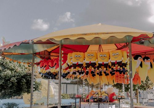 A vibrant fairground stall with plush toys including popular characters on display under a canopy.