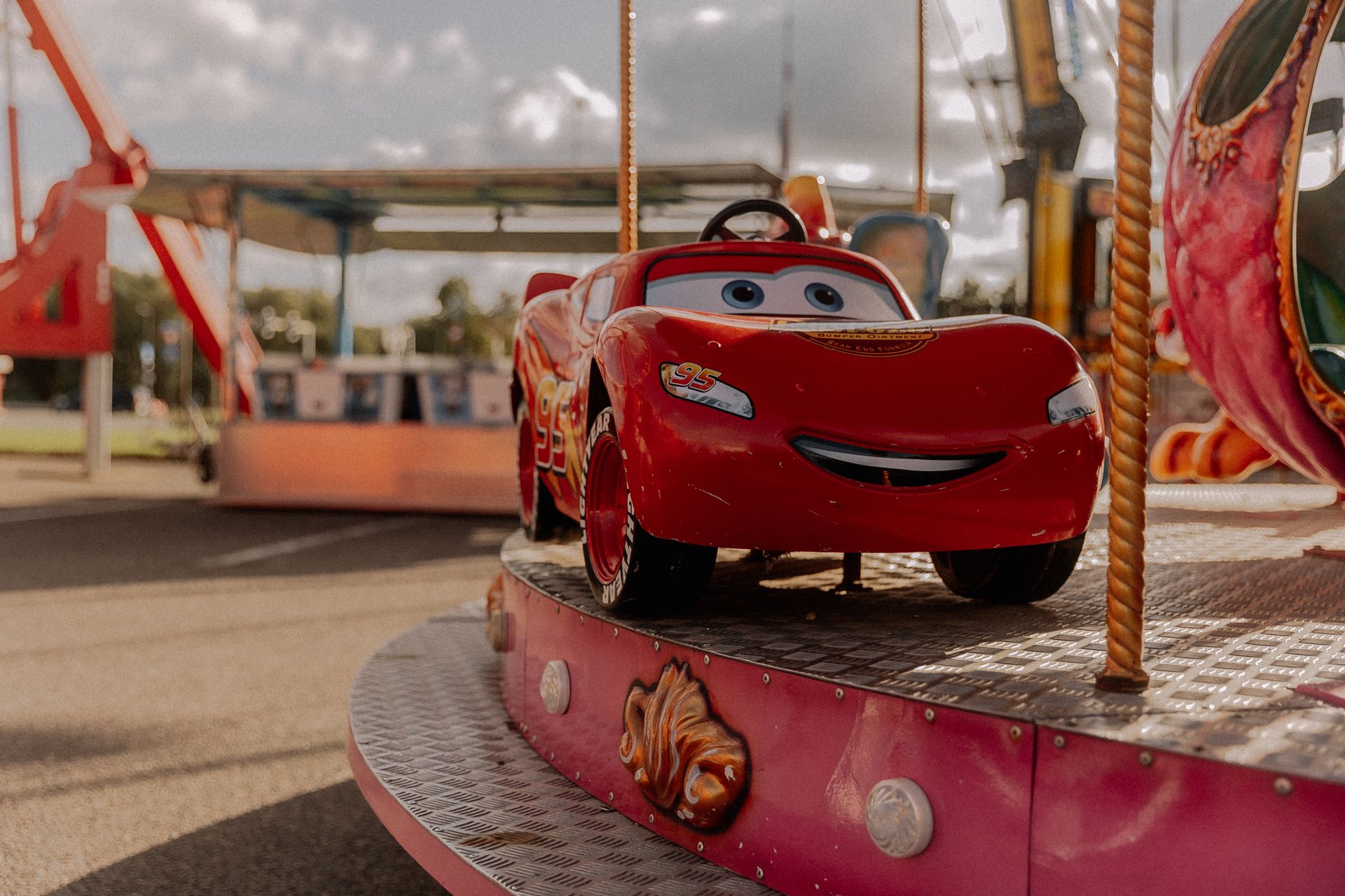 Bright red car-themed ride on an outdoor carousel during a sunny day in a theme park.