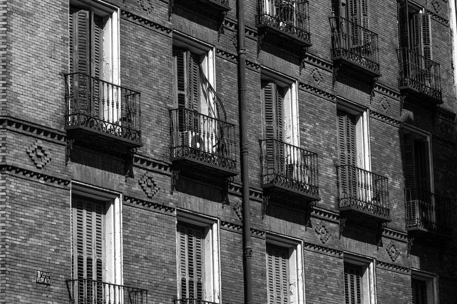 Foto en blanco y negro de la fachada de un edificio de apartamentos en Madrid, con balcones clásicos y mampostería intrincada.