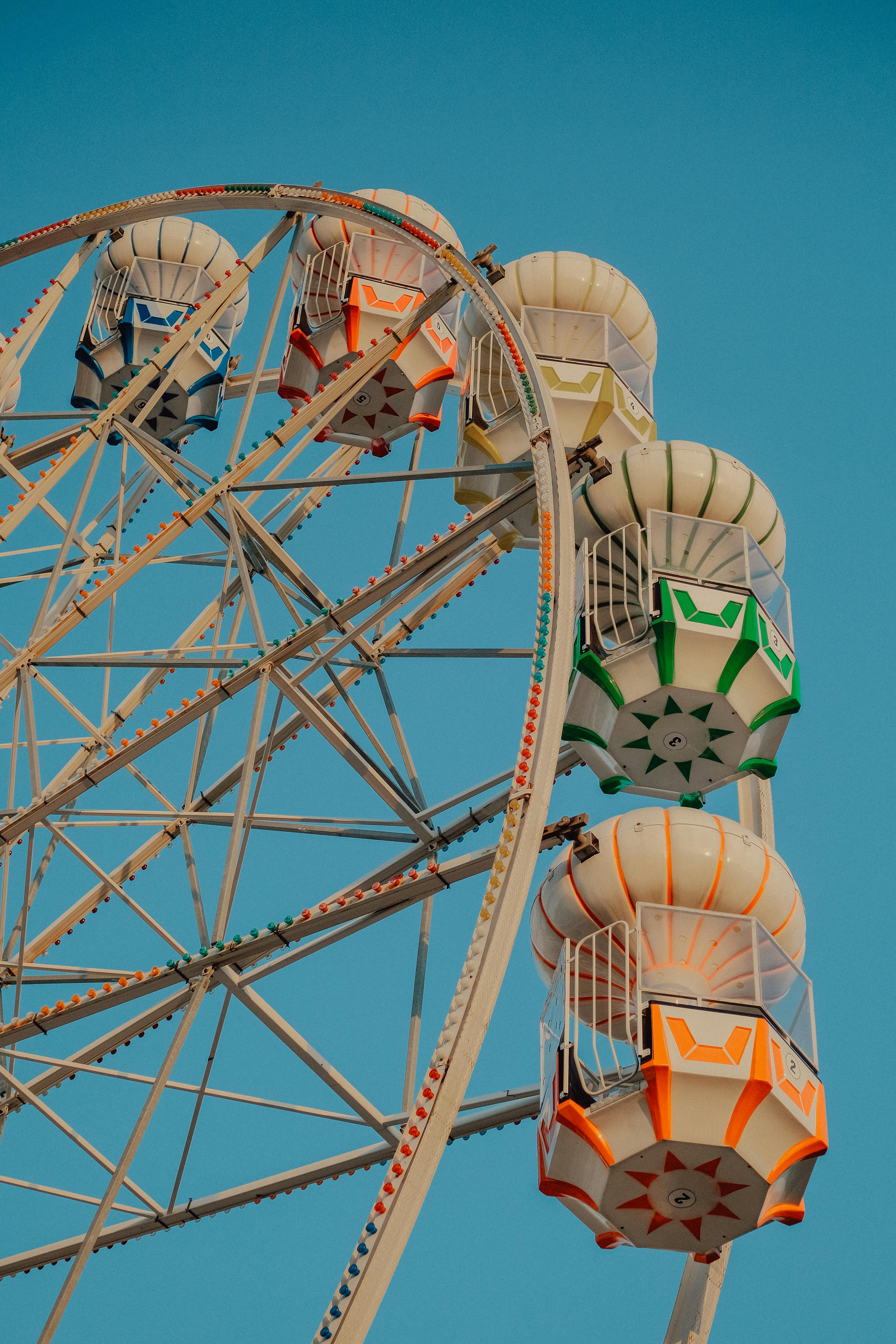 A vibrant ferris wheel with multicolored cabins set against a clear blue sky, capturing a funfair atmosphere.