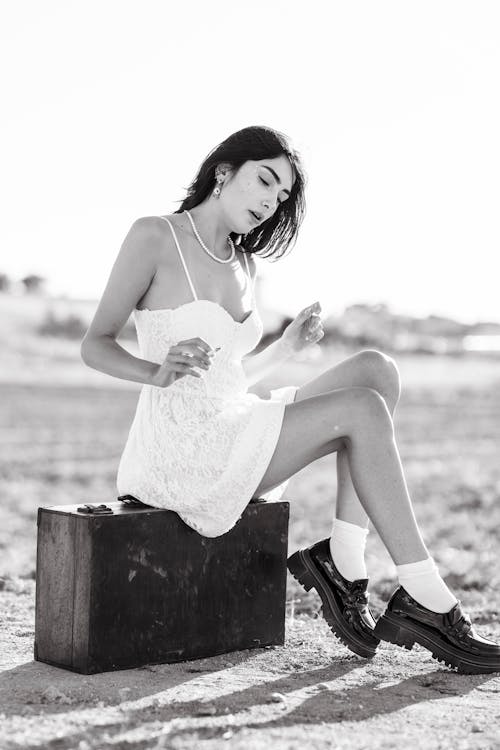 Brunette Woman in White Mini Dress Sitting on a Wooden Suitcase