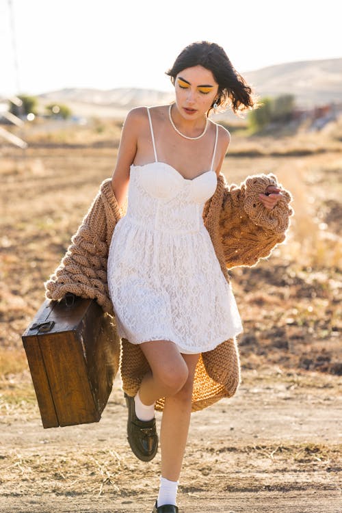 Young Woman in White Lace Mini Dress Carrying a Vintage Wooden Suitcase