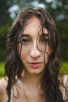 Close-up of a young woman with wet hair in an outdoor setting, showcasing natural beauty and serene expression.
