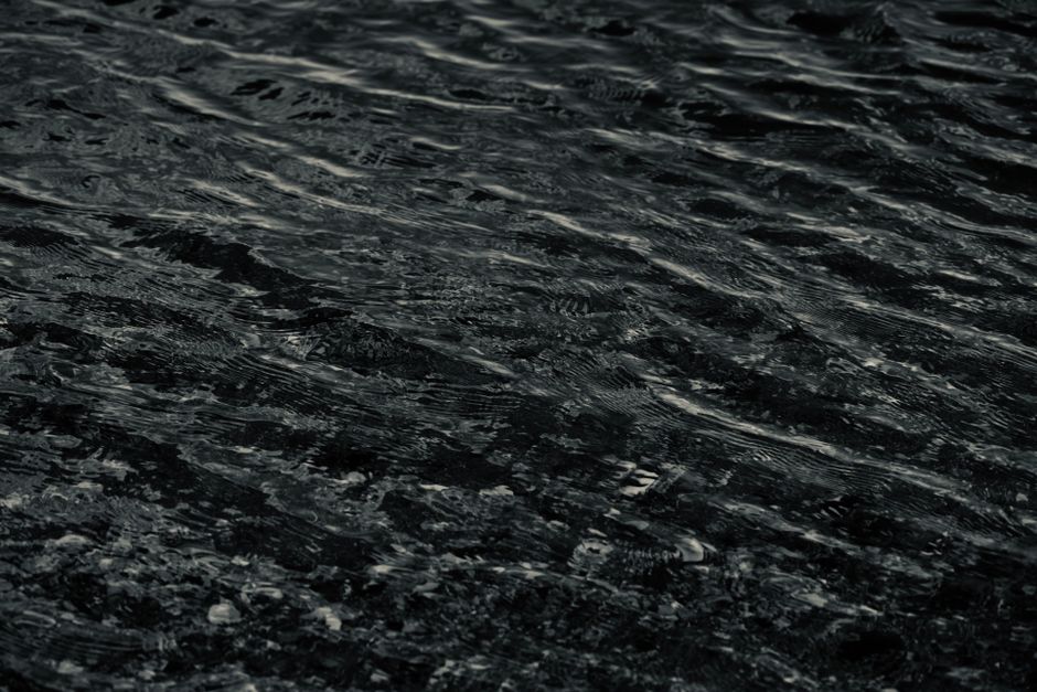 A moody close-up of dark wavy water texture, showcasing natural patterns and reflections.