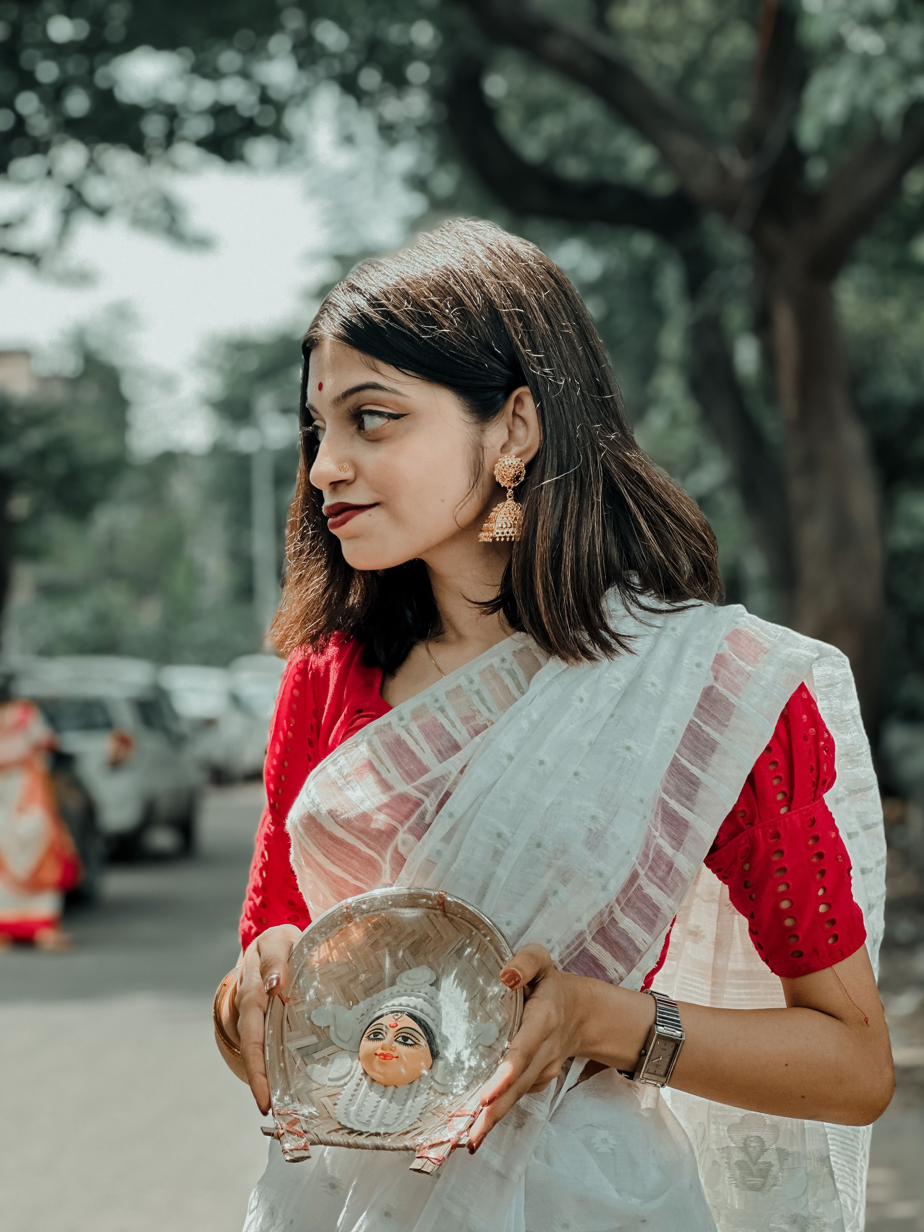 A woman in a traditional Indian sari holding a decorative bowl outdoors in Kolkata, India.