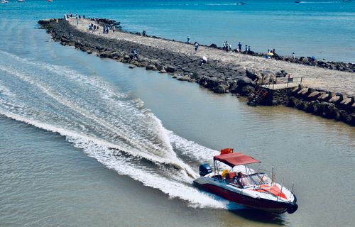 Free Aerial view of a red motorboat speeding along a rocky pier with people enjoying a sunny day by the sea. Stock Photo