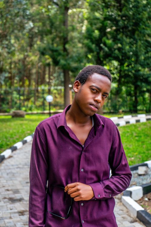 Free Young man in a purple shirt posing outdoors with sunglasses, exuding confidence. Stock Photo
