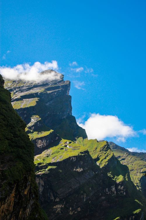 Free Vertical view of a rocky mountain peak with clouds under a clear blue sky, showcasing nature's beauty. Stock Photo