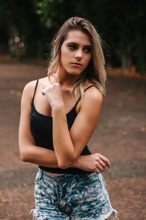 Free Beautiful young woman posing in denim shorts and camisole in a casual outdoor setting. Stock Photo