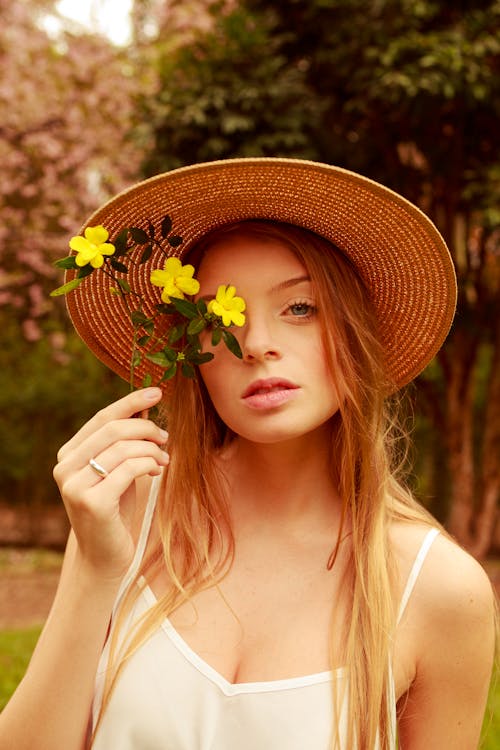 Woman Wearing Straw Hat Holding Yellow Flowers Near Her Face