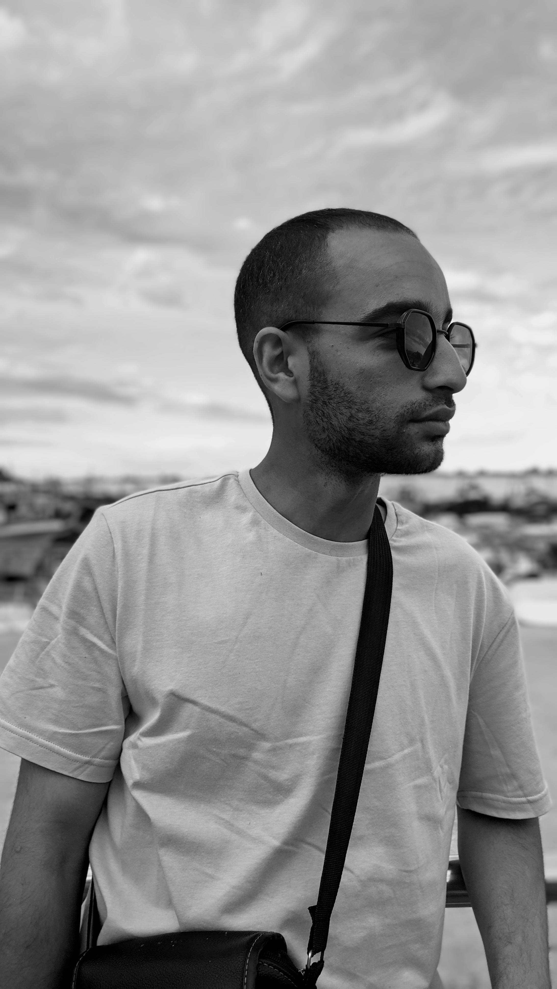 Black and white portrait of a young man wearing sunglasses and a t-shirt with a scenic background.