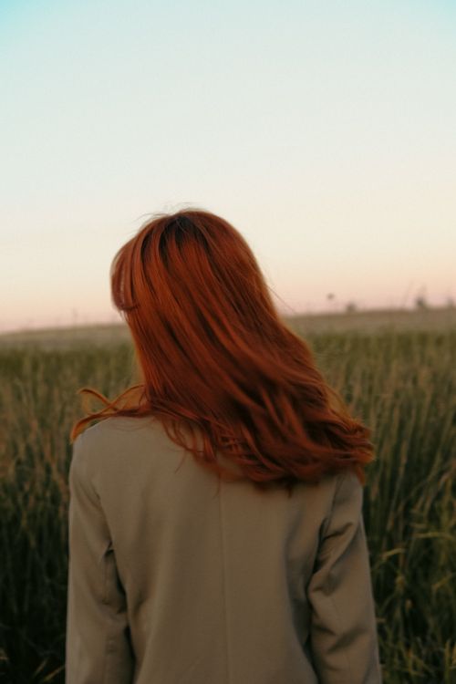 Free Elegant woman with red hair in olive blazer standing in rural field at sunset. Stock Photo
