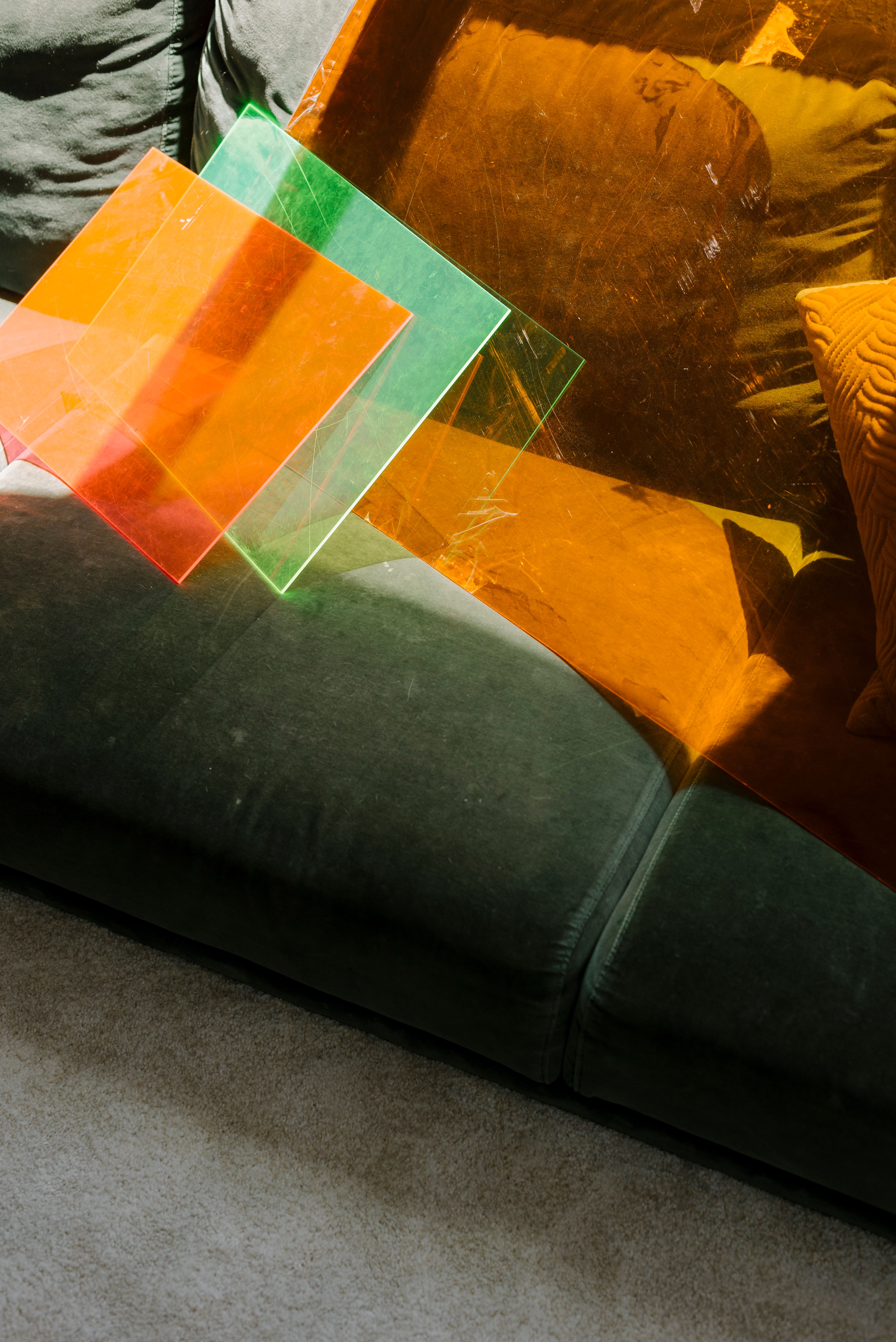 Bright acrylic sheets casting colorful shadows on a green sofa with cushion. Artistic and vibrant scene.