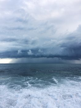 An intense storm approaches over the ocean with dark clouds and splashing waves.