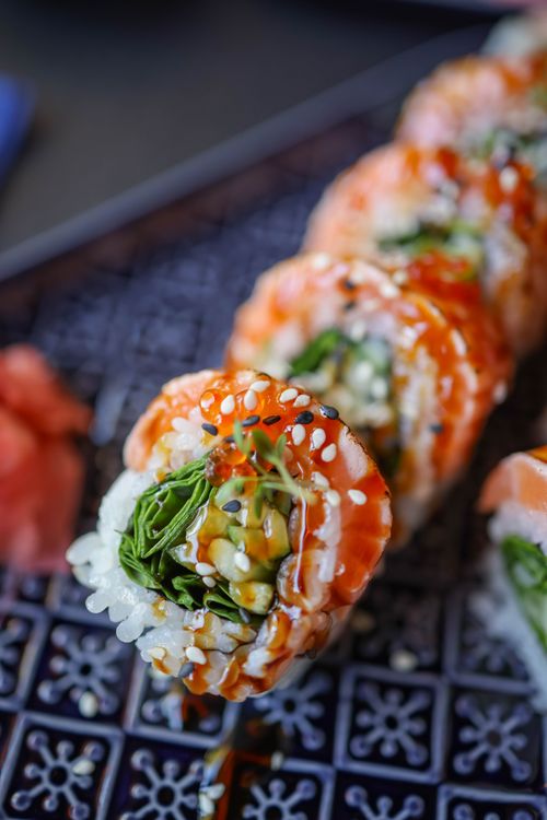 Free Close-up of vibrant sushi rolls featuring fresh vegetables and salmon, beautifully plated with sauce. Stock Photo