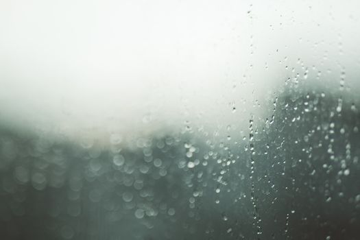 Close-up view of a window with raindrops and a soft bokeh background, creating an abstract texture.