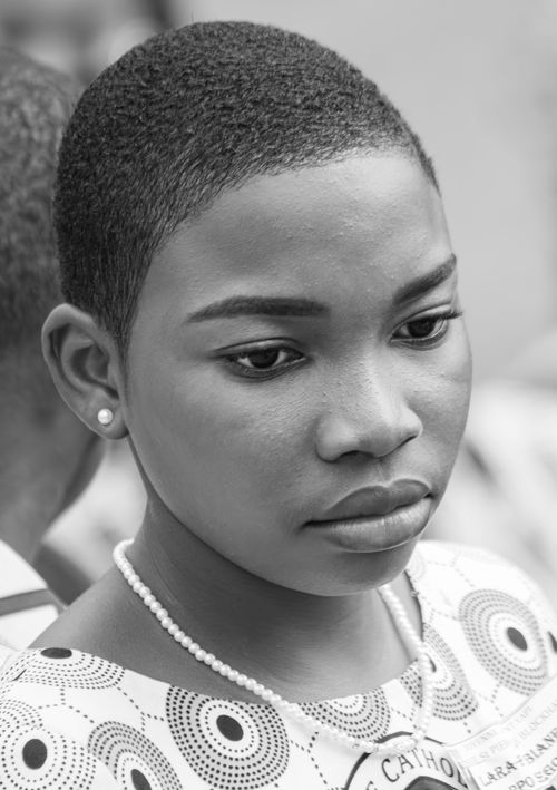 Free A close-up black and white portrait of a young woman with short hair and a pearl necklace, deep in thought. Stock Photo