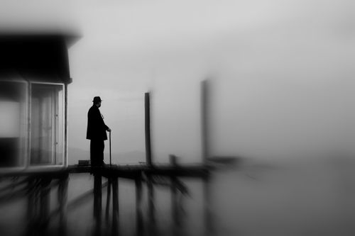 Free Silhouette of an elderly man with a cane on a foggy pier, in black and white. Stock Photo
