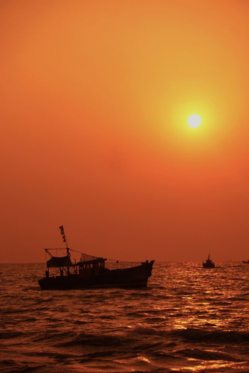 Free Silhouetted boat drifting on a dramatic sea at sunset, with a vibrant orange sky. Stock Photo