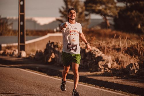 Free A cheerful man runs down a city street during a marathon, exuding energy and determination. Stock Photo