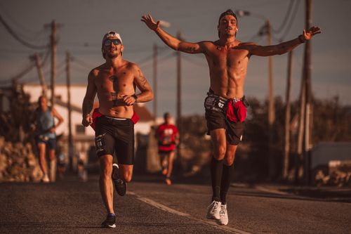 Free Two men running energetically shirtless on urban streets during the day. Stock Photo