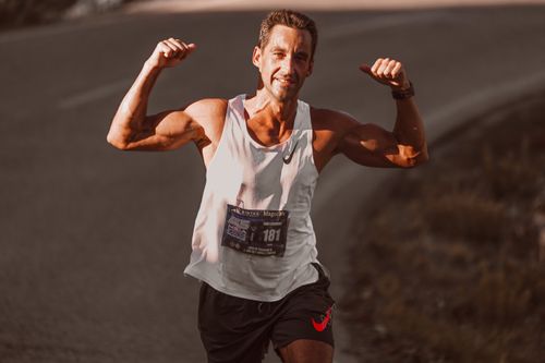 Free Male runner with arms raised celebrating success during a city street race on a sunny day. Stock Photo