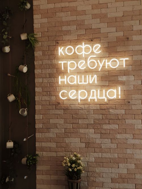Free Cozy coffee shop interior featuring a neon sign with Russian text on a brick wall. Stock Photo
