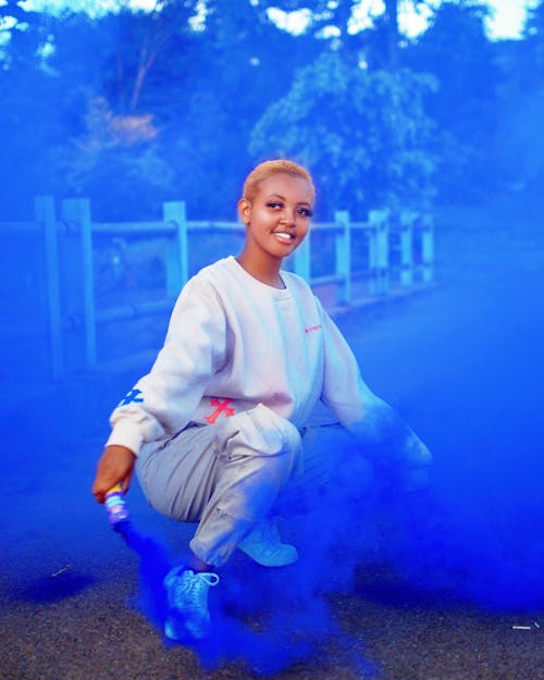 Young Woman Holding a Blue Smoke Flare and Smiling