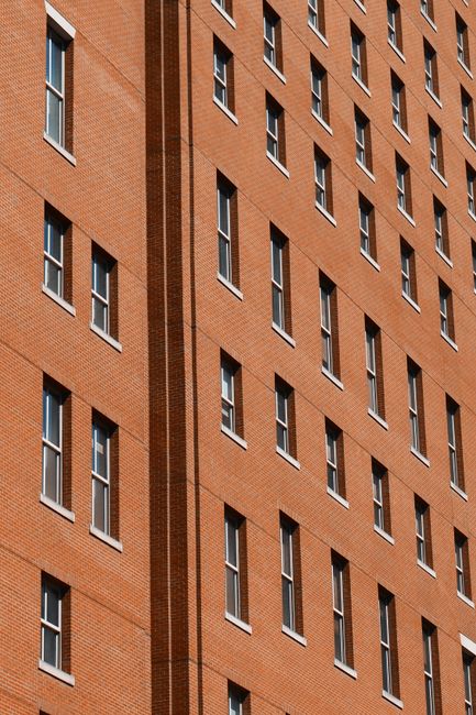 Diagonal view of a red brick building facade with rows of windows in New York City.