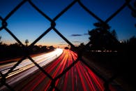 日落时分，高速公路上车辆驶过链条围栏，留下动态的光影轨迹