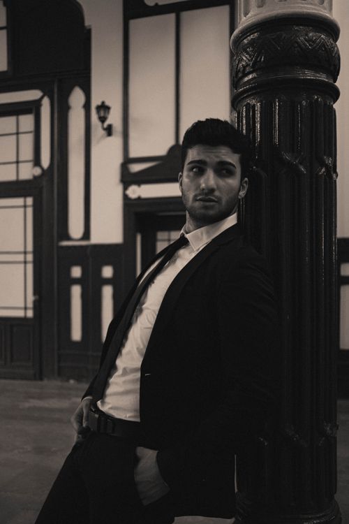 Free Stylish black and white portrait of a man in a suit leaning against a column indoors. Stock Photo