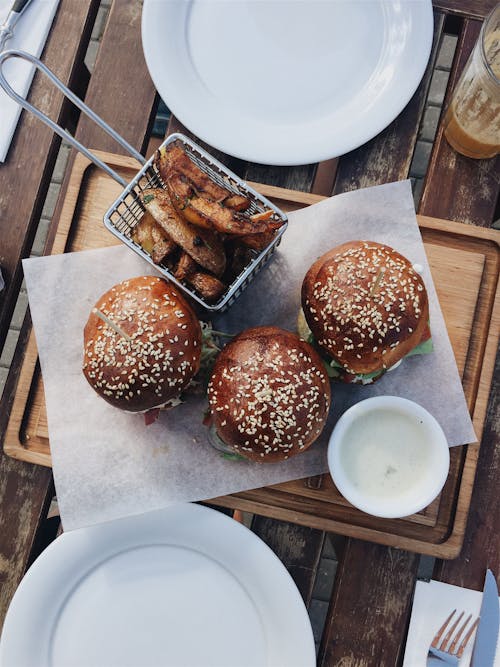 Three Burgers on Brown Wooden Tray Between White Ceramic Plate