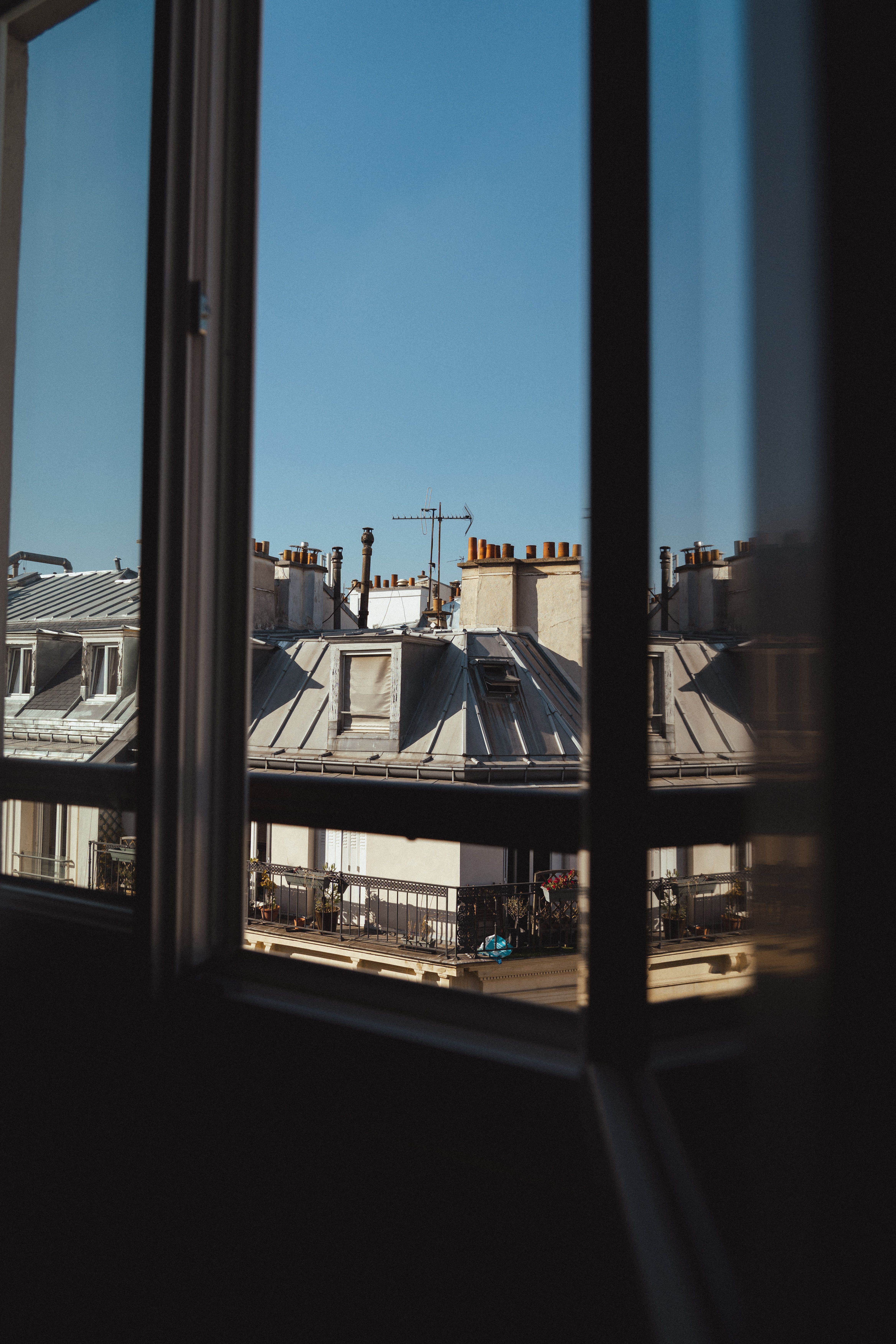 Framed view of urban rooftops captured through a window under a clear blue sky.
