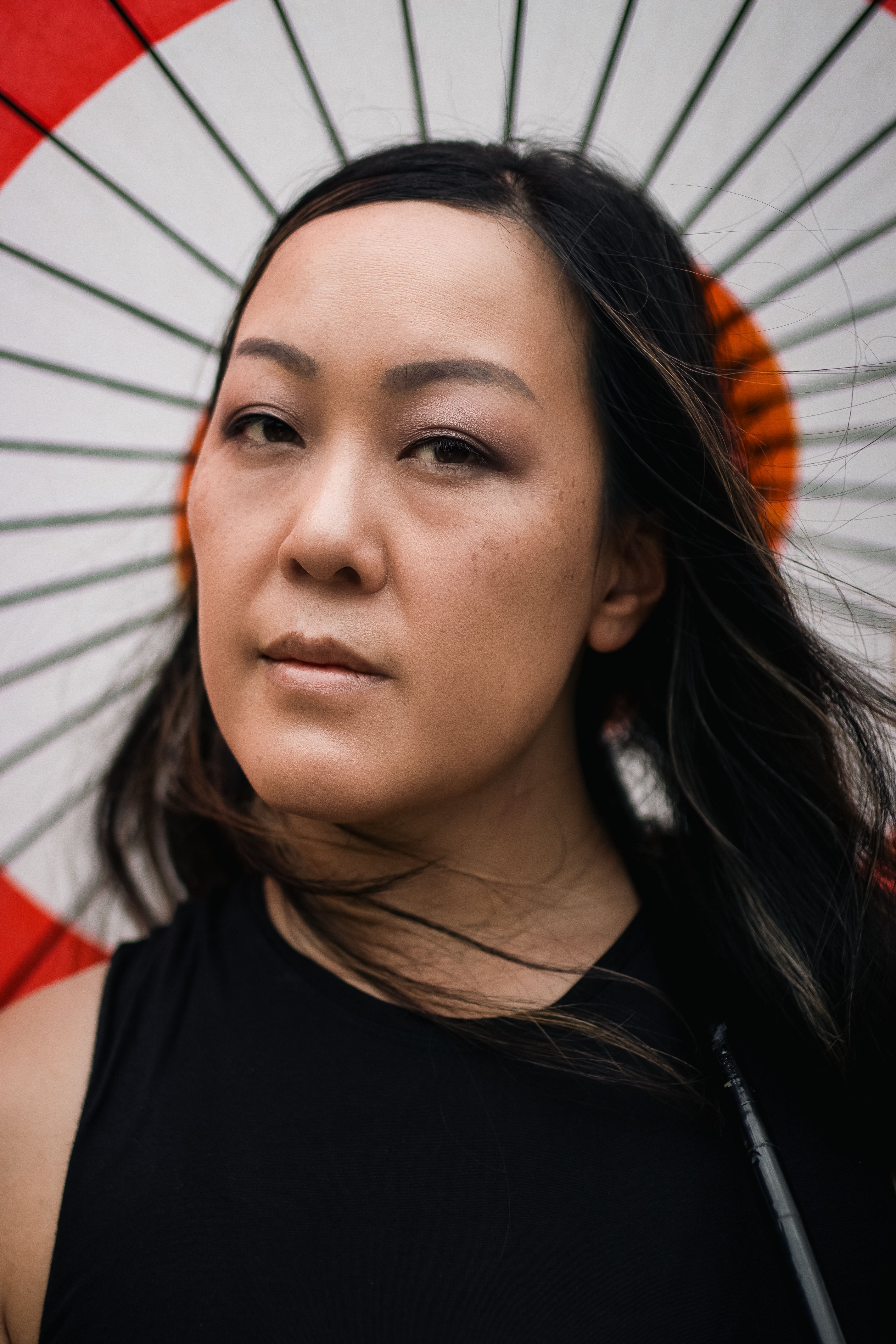 Engaging portrait of a woman standing under a Japanese parasol. Expressive eyes and long hair.
